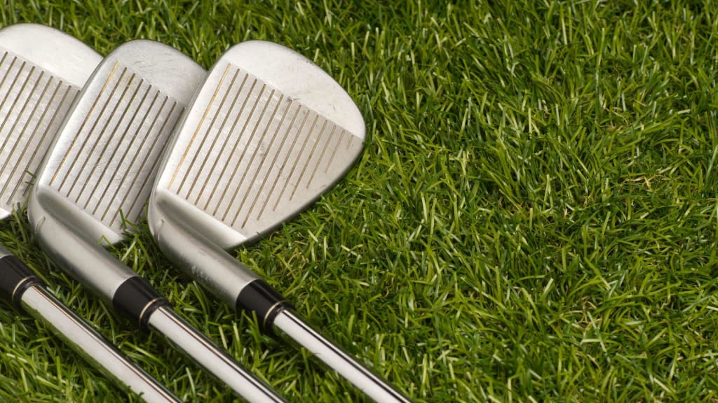 Three golf clubs, known as the most forgiving golf irons, are gracefully resting on the lush green grass.